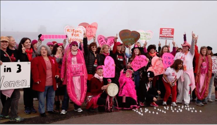 A photo of a bunch of women dressed in pink, some are in vagina costumes and holding sign like: Rising for justice, 1 in 3 women...