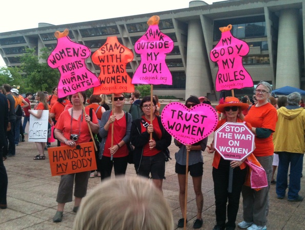 A group of 6 women holding signs shaped like a womens body with writing that says: Women's rights equals human rights!, Stand with texas women, Think outside my box! My body my rules.