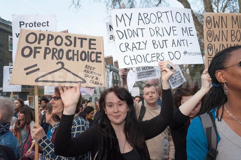 A photo of an abortion protest with some signs that say: Opposite of prochoice = Coat Hanger, and My Abortion didnt drive me crazy but anti-choicers do