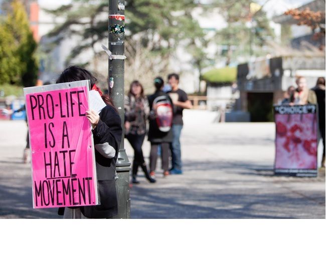 A photo of a display of graphic abortion photos where a single female student holds a sign further away that says: Pro-Life is a HATE movement