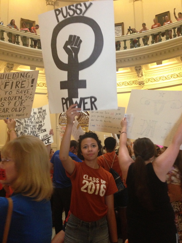 A photo of a young female in the Texas state capital in Austin Texas holding a sign that says: P***Y Power