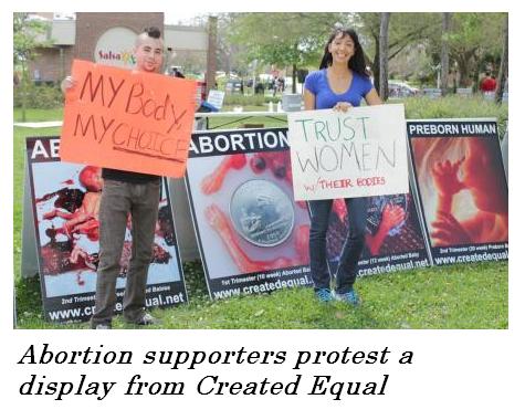 Abortion supporters protest a display from Created Equal holds signs that say: Trust women w/their bodies. A male is holding one that says: My Body My Choice