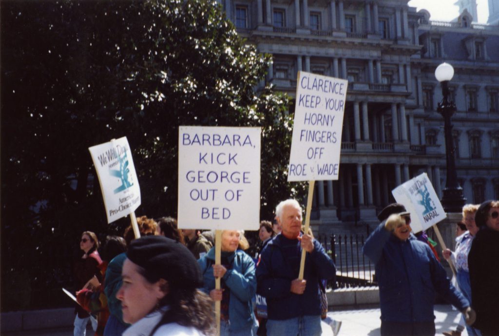 An elderly couple are at an abortion protest and both are holding signs that say: Barbara, Kick George out of bed and Keep your horny fingers off Roe v. Wade