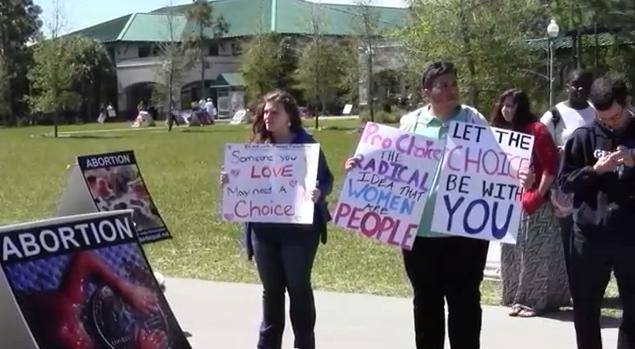 A graphic abortion photos display where counter protesters are holding signs that say: Someone you love may need a choice, Pro Choice the radical idea that women are people, Let the choice be with you