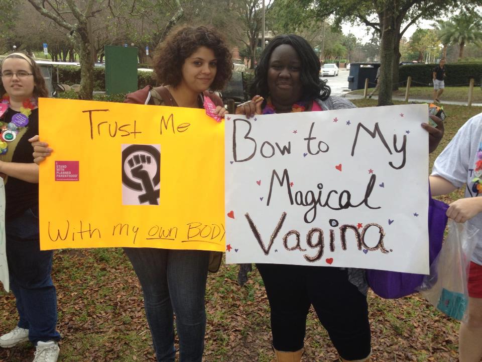 Two female protesters hold signs that say: Trust me with my own body, and Bow to my Magical Vagina