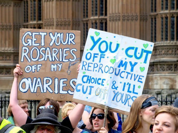 A photo of two protest signs that say: Get your Rosaries off my Ovaries, and You cut off my reproductive choice and I'll cut off yours