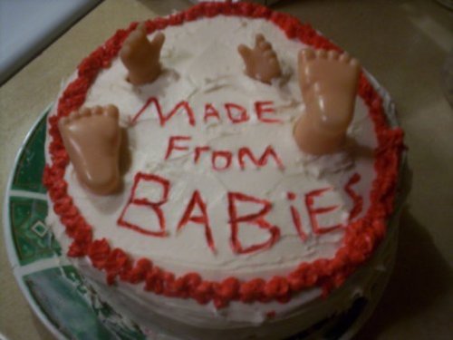 A photo of a home made cake with baby doll hands and feet sticking up out of the frosting with the writing of Made From Babies on it