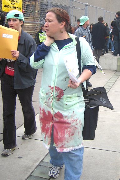 A photo of a female at an abortion rally wearing a bloody doctors coat with a coat hanger