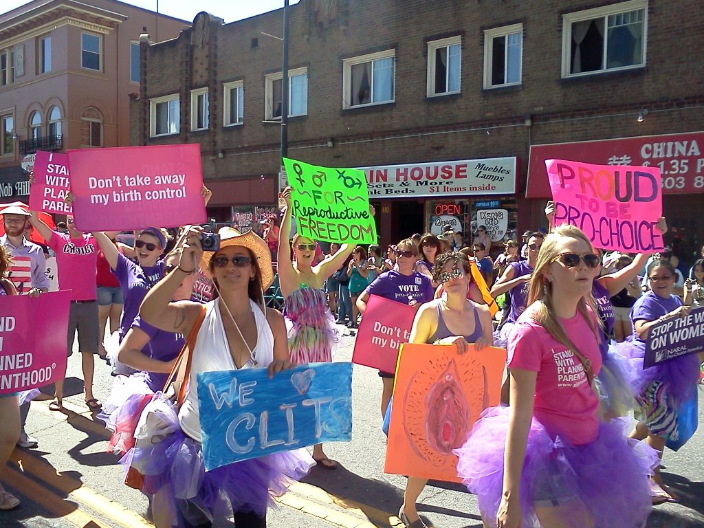 A photo from Pro-Choice Colorado when they were in the PRIDE parade. Some girls are wearing purple tutu's and holding signs that say We Heart Clits and PROUD to be pro-choice