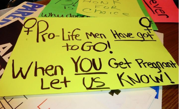 A photo of a stack of posters and the top one says: Pro-Life men have got to go! When you get pregnant let us know!