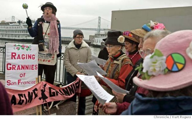 A photo of the Raging Grannies of San Francisco. They are older women wearing scarfs, big hats, wearing flowers, tons of pins and bright colors