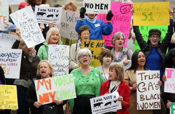 A photo of an abortion protest in Georga of women all holding different protest signs and shouting! Some signs say: My Voice My Choice, Trust GA's Black Women, We are the 51%...