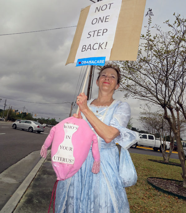 A picture of a women in a cinderella costume holding a sign that says: Not One Step Back and holding a homemade uterus that says: Who's in your uterus?