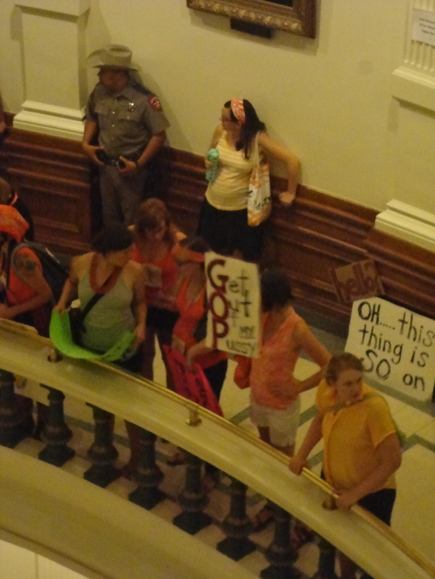 A photo inside the Texas state capital and a women is holding a sign that says: Get Out Of my P***Y