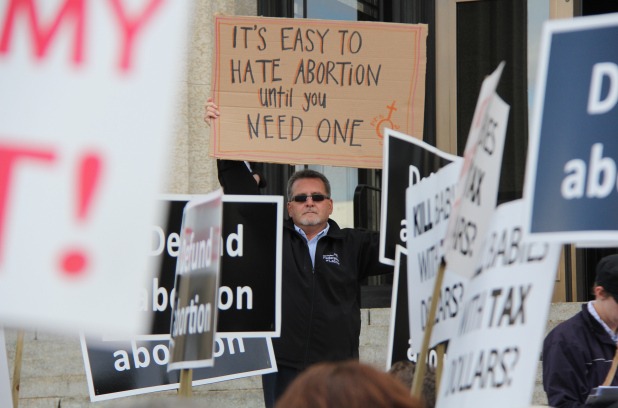A photo of a man holding a handmade sign that reads: It's Easy to Hate abortion untill you need one