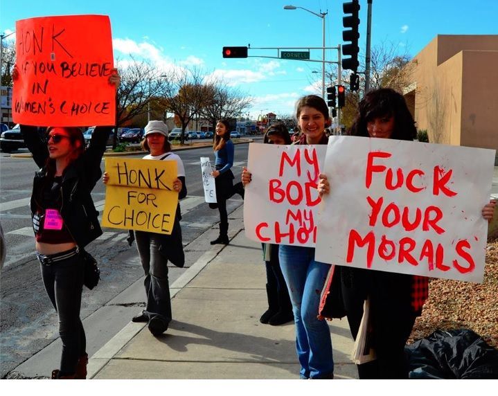 Photo of a few young females holding signs that say: F**K your Morals, My Body My Choice, HONK if you believe in womens choice
