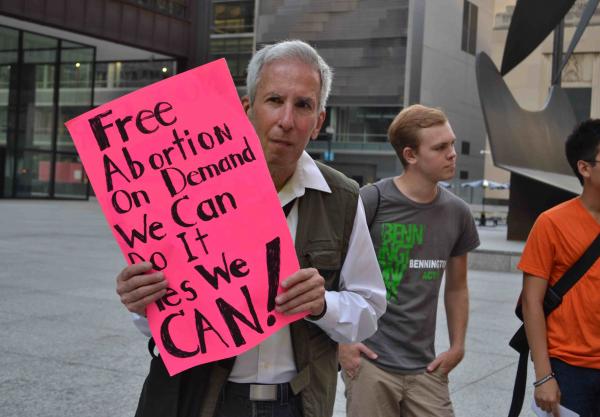 A photo of a elderly man carrying a sign that says: Free Abortion on demand we can do it yes we can!