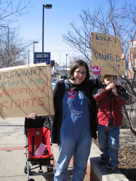 A mother and her young son are holding signs that say: Pregnany mom for abortion rights, Every child a wanted child!