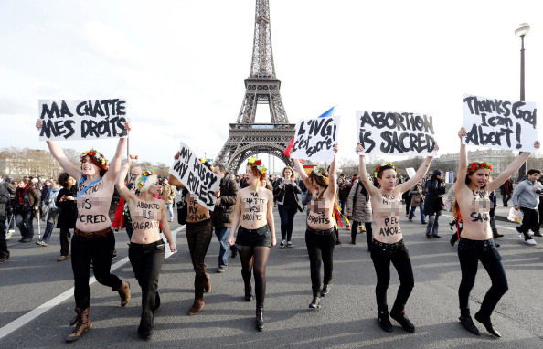 Photograph of seven topless women in front of the Eiffel Tower in France with signs that read: Abortion is Sacred or Thanks God I can abort! My pussy my rules