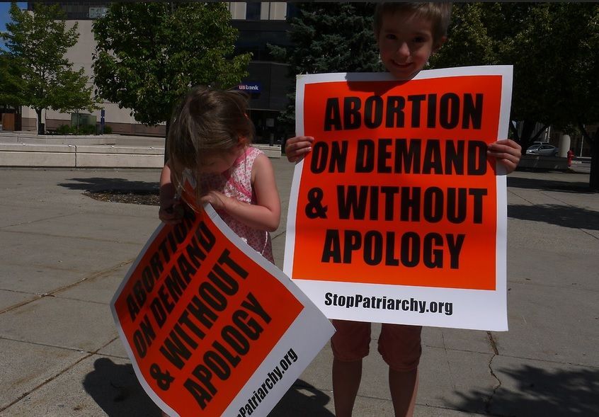 Two very young kids a boy and a girl holding Stop Patriarchy's sign that says: Abortion on demand and without apology