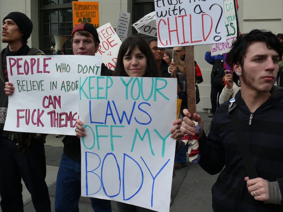 A photo of a group of abortion protesters with signs that say: Keep your laws off my body and People who dont believe in abortion can F**K themselves