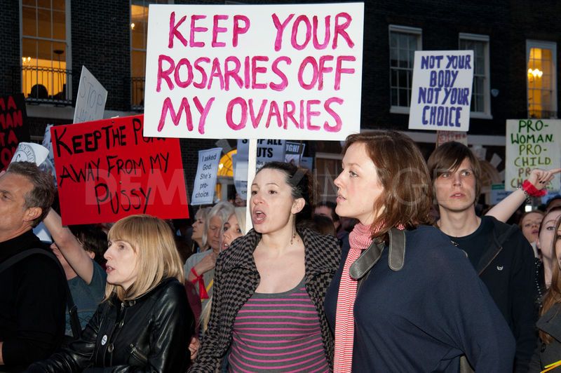 A group march with angry women shouting and holding signs that read: Keep the pope away from my P***y, Keep your rosaries off my ovaries, Not your body Not your choice