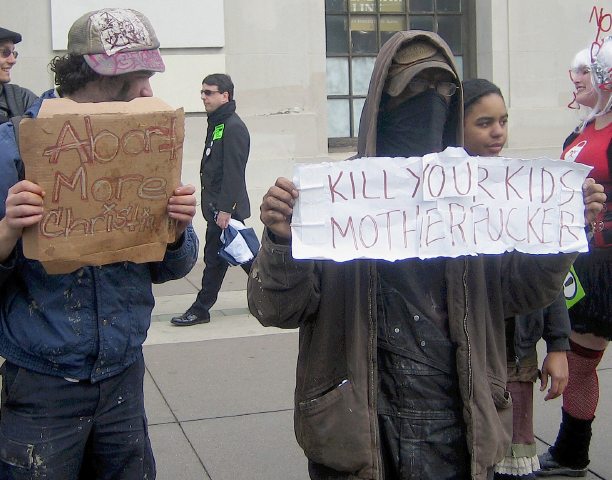 A picture of pro-choice boys from an anarchist group holding signs saying: Abort more christians, Kill your kids motherf***ers