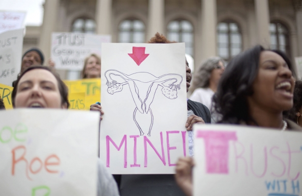 A photo of an abortion rally where one female is holding a sign with a hand drawn female reproductive system on it saying MINE!