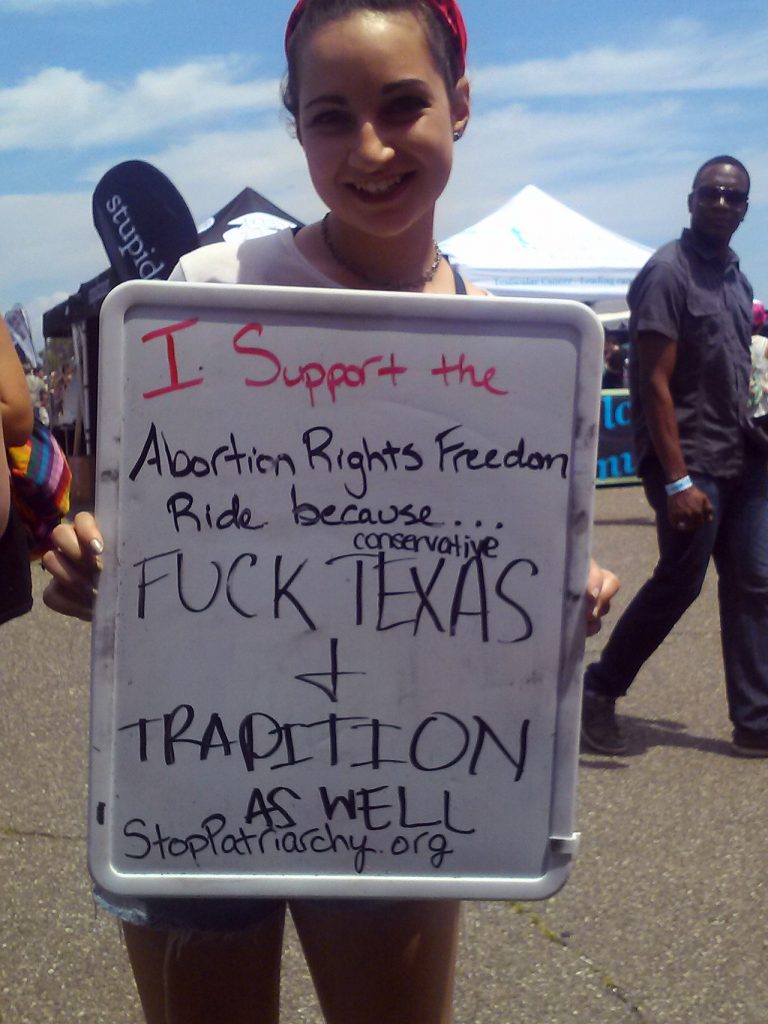 A picture of a young female holding a sign that says: I support the Abortion Rights Freedom Ride because...F**K Conservative Texas and Trapition as well