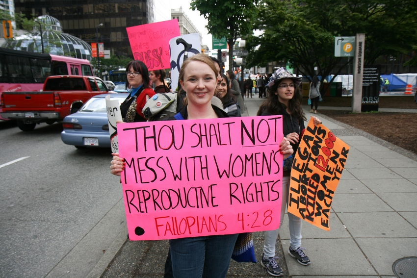 A picture of a young women at an abortion rights rally with a sign that reads: "Thou shalt not mess with womens reproductive rights Fallopians 4:28"