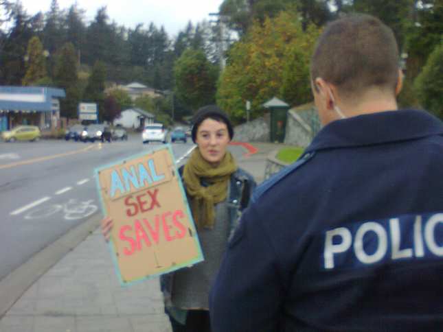 A picture of a women abortion protester who is getting arested for holding this sign: "Anal Sex Saves"