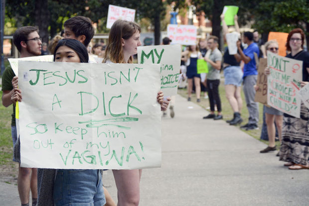 A picture of a student protesting a pro-life demonstration with a sign that says "Jesus isn't a dick so keep him out of my vagina"