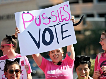 Woman with cat face paint holds a sign which reads, "Pussies Vote."