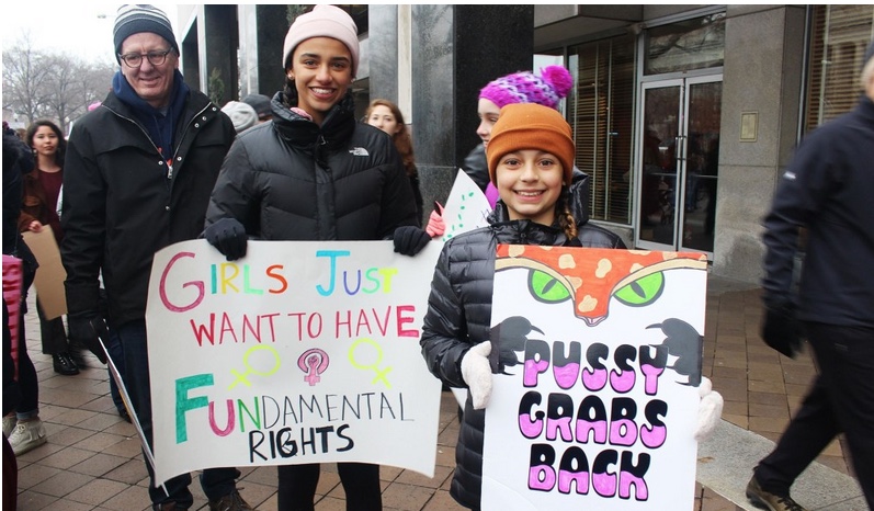 Young girls hold signs reading, "girls just want to have fundamental rights," and "Pussy grabs back."