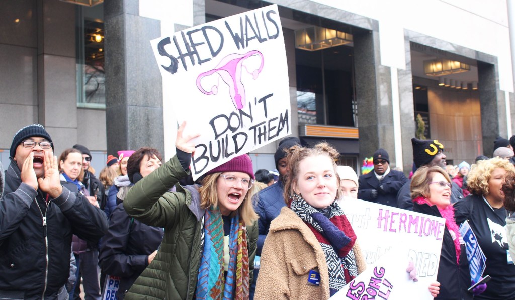 Woman holds up sign which reads, "shed walls don't build them."