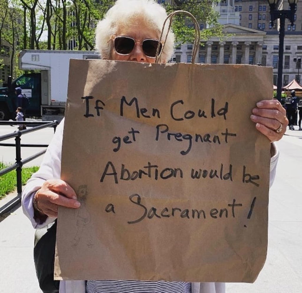 Older woman holds up a paper bag with writing on it that says, "If men could get pregnant abortion would be a sacrament!"