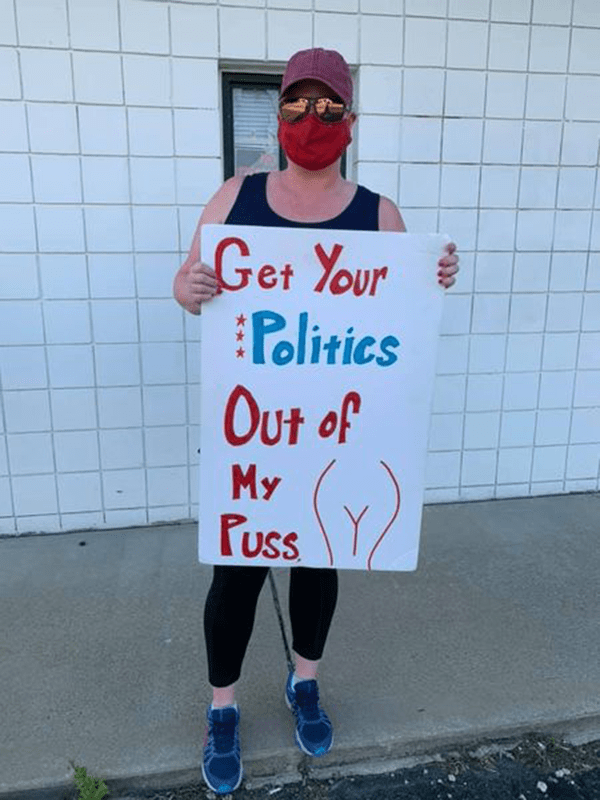 Person holding a sign which reads, "Get your politics out of my puss."
