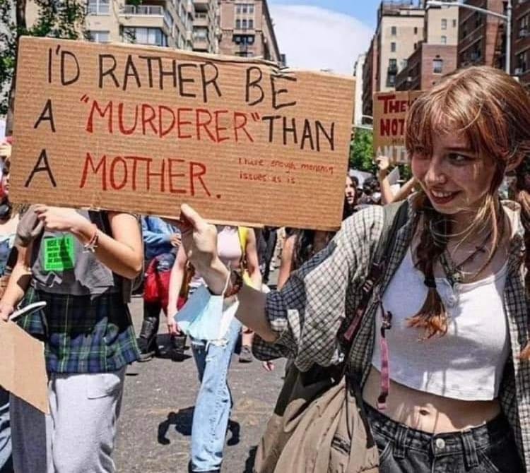 Young woman holding a cardboard sign that reads, "I'd rather be a "murderer" than a mother. I have enough mother issues as is."