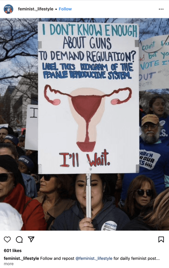 Woman holding a sign which reads: "I don't know enough about guns to demand regulation? Label this diagram of the female reproductive system. (Poorly painted picture of uterus and Fallopian tubes) I'll wait."